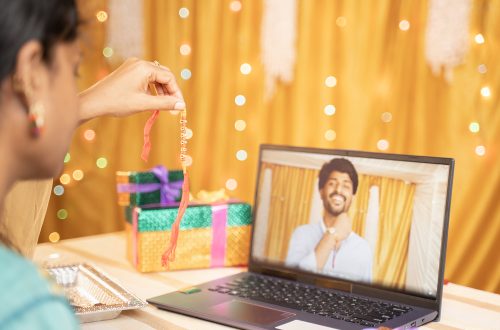 a girl showing her brother a rakhi through a laptop