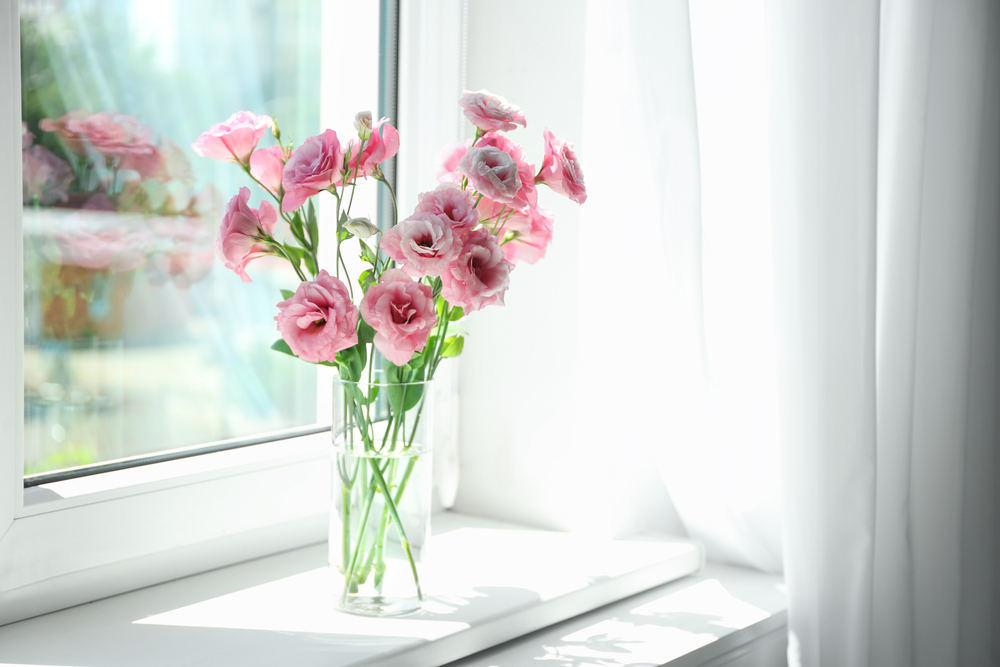 pink roses inside a glass vase on a window sill