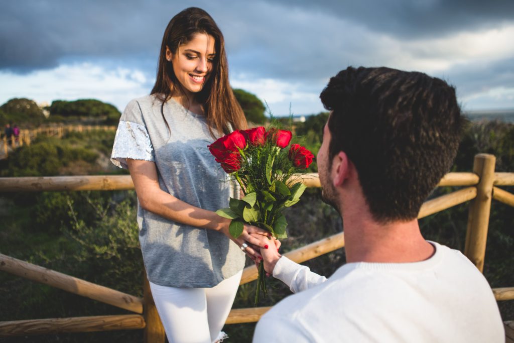 man kneeling handing bouquet roses woman1