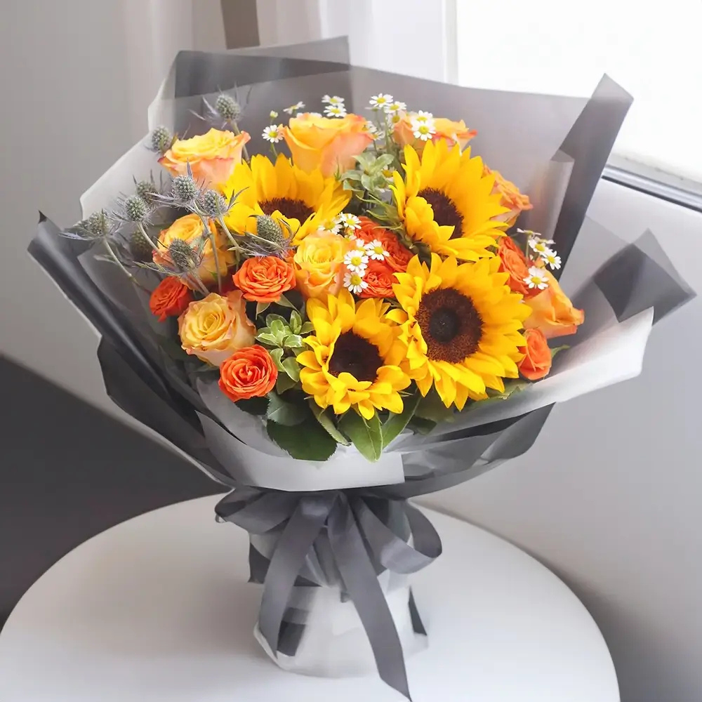 Sunflowers and Roses: The Right Mix for Every Occasion 3 Sunflowers and Roses bouquet arranged with orange and yellow blooms, white daisies and greenery, wrapped in grey paper.